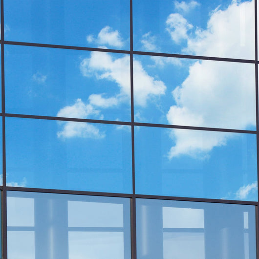 A modern building with a spacious glass window reflecting the serene sky.